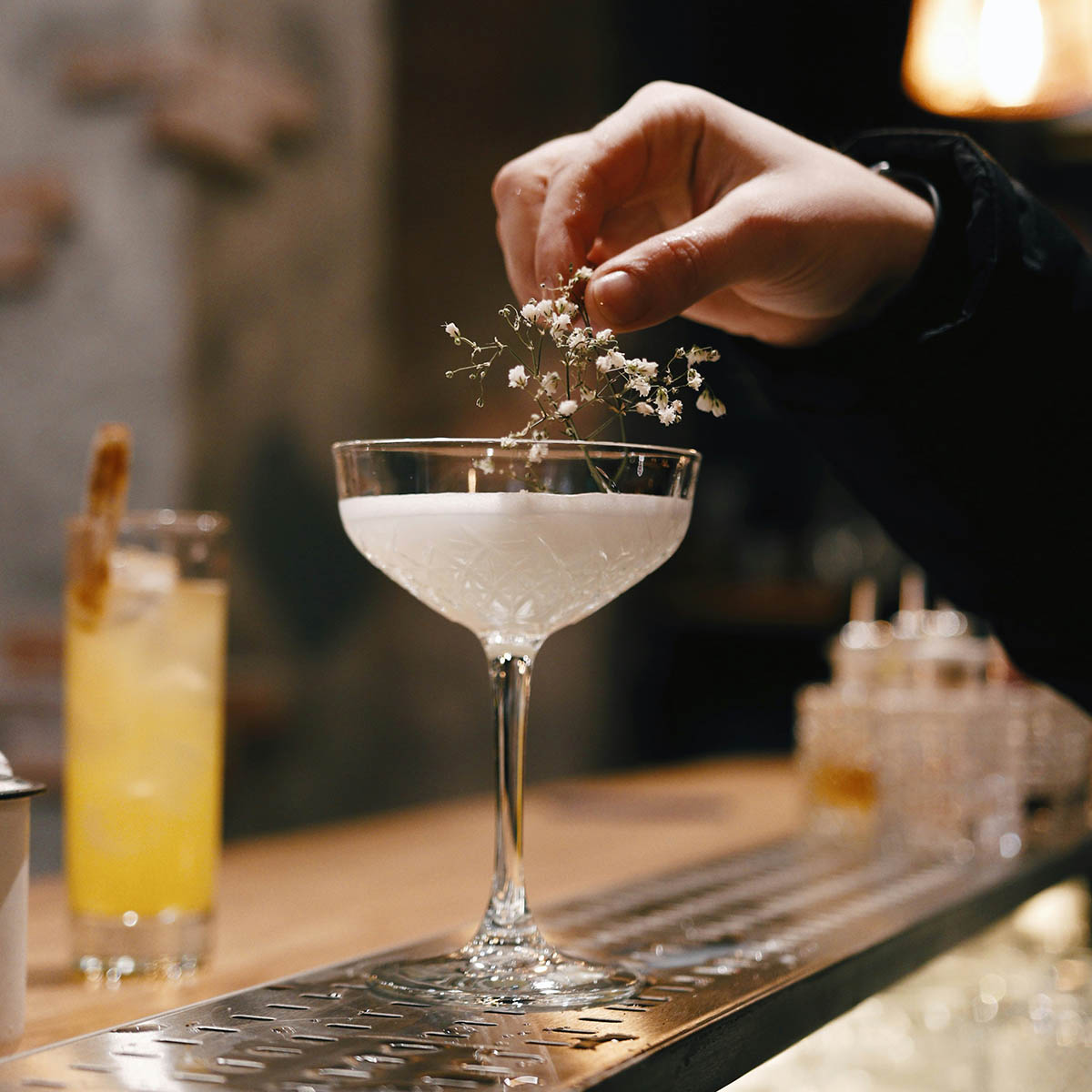 Person making craft cocktail in glass with sprig of fresh herb.