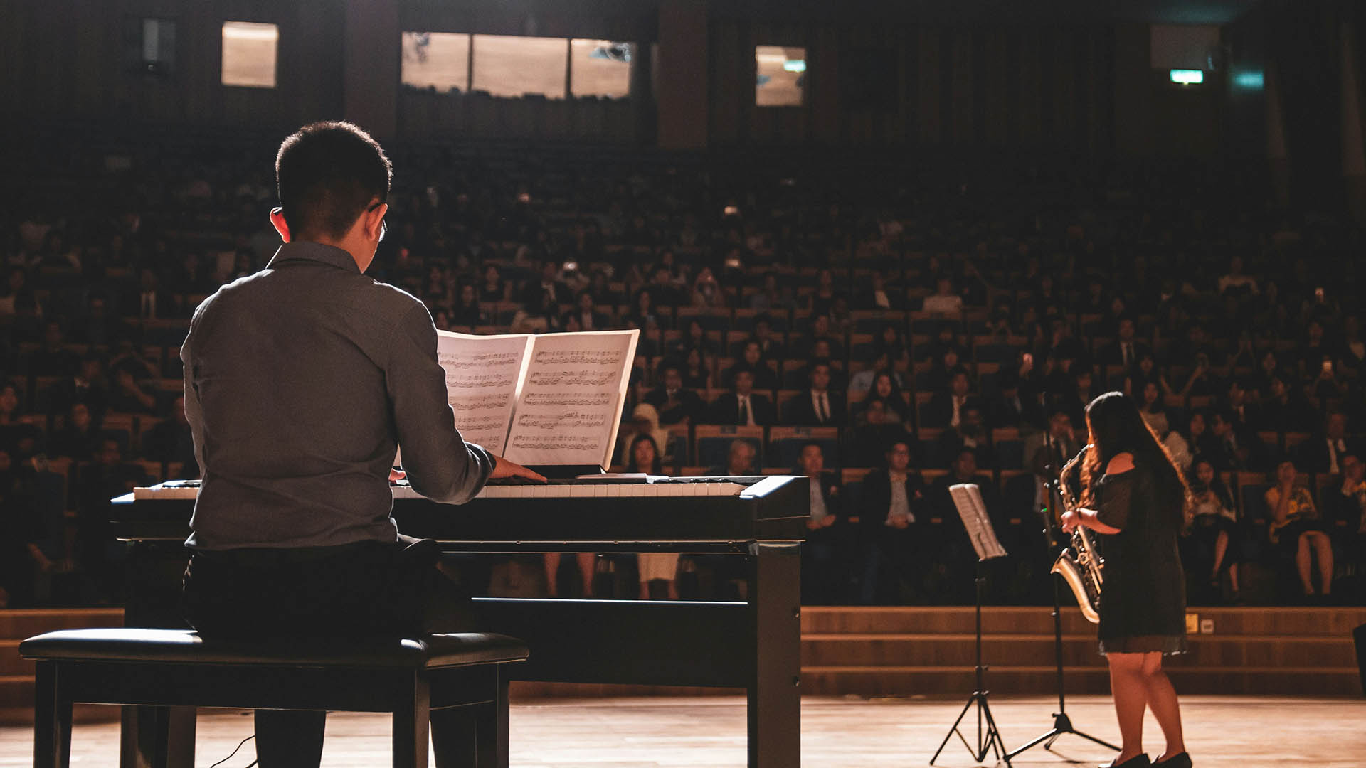 Musical performers playing piano and saxophone in front of an audience.